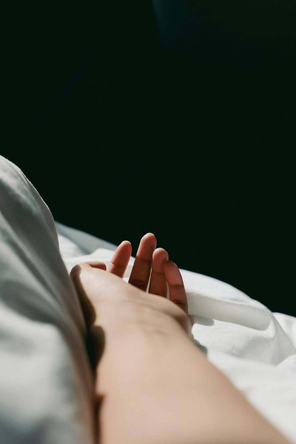 A hand resting on bed sheets in soft daylight.