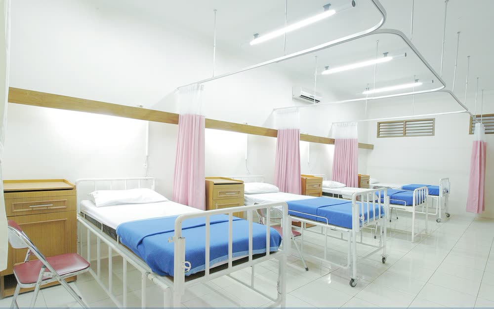 An empty hospital ward with made beds and drawn curtains.